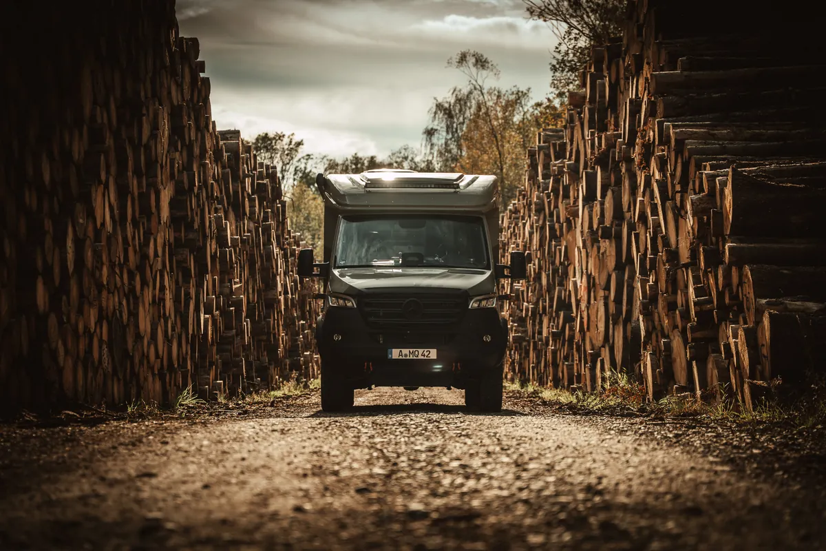 HYMER MLT 580 zwischen hohen Holzstapeln auf einem Waldweg